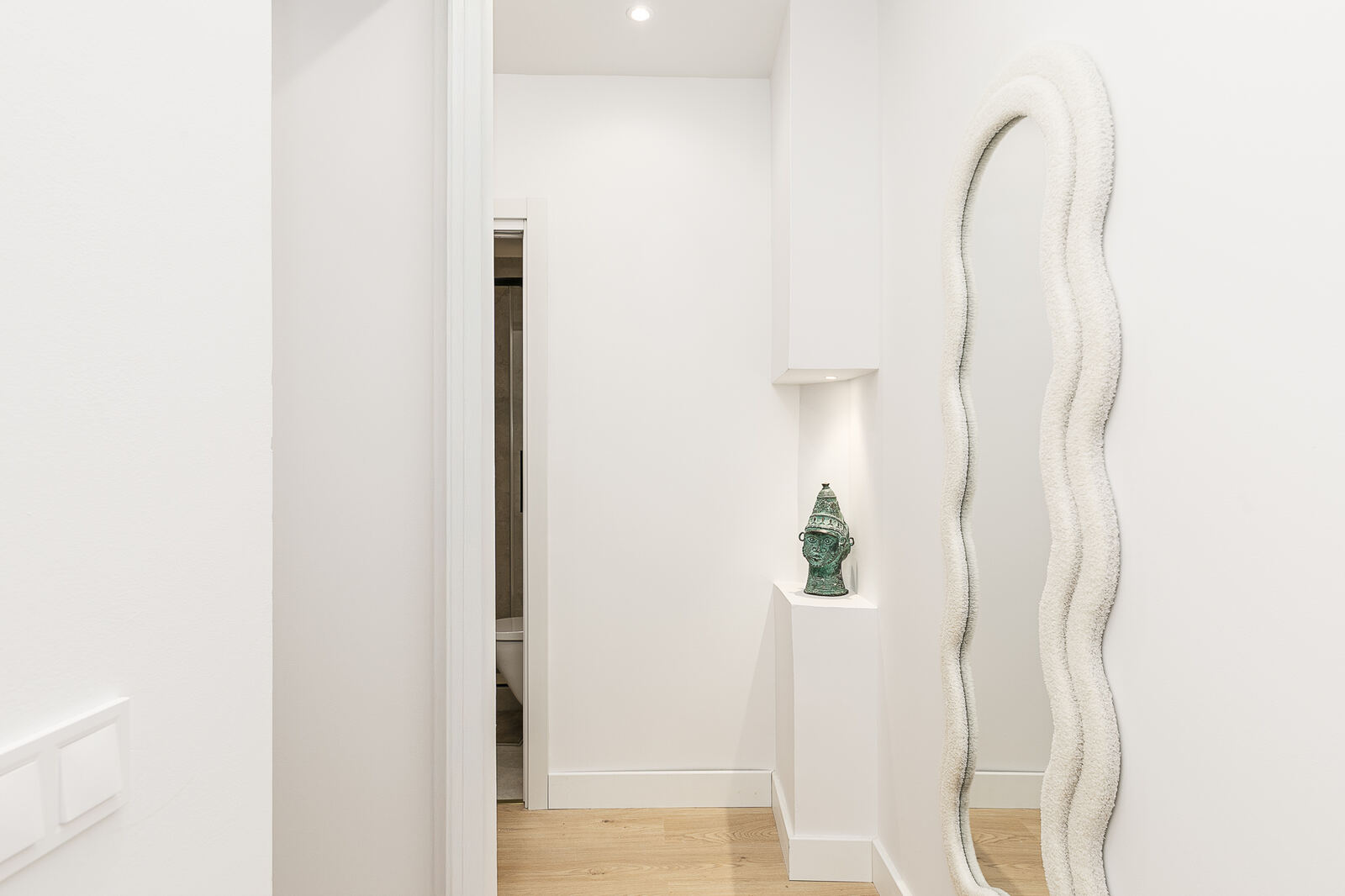 Entry hallway after renovation — clean white plaster, sculptural mirror, oak floor